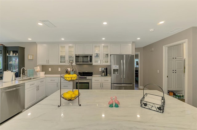 kitchen featuring a sink, appliances with stainless steel finishes, white cabinets, and light stone counters