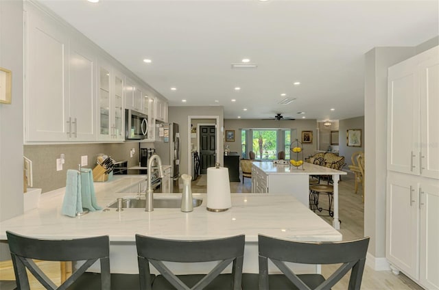 kitchen featuring a peninsula, glass insert cabinets, ceiling fan, a kitchen bar, and appliances with stainless steel finishes