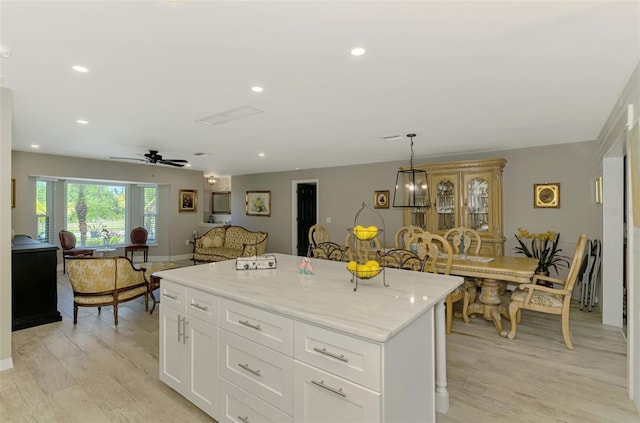 kitchen with a center island, light stone counters, light wood-type flooring, and white cabinetry