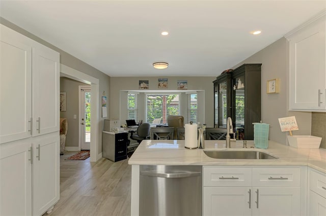 kitchen with stainless steel dishwasher, a peninsula, light wood-type flooring, white cabinetry, and a sink