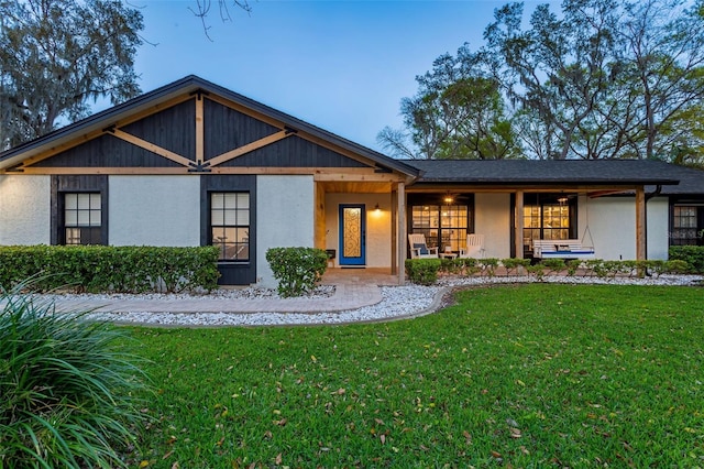 view of front of house with stucco siding, covered porch, and a front lawn