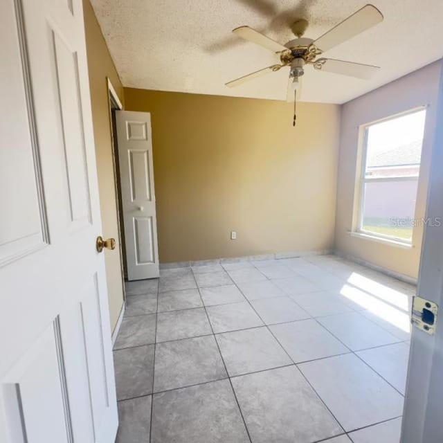 empty room featuring a textured ceiling, ceiling fan, and light tile patterned floors