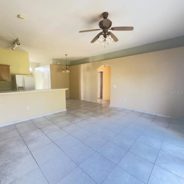 unfurnished room featuring baseboards, arched walkways, ceiling fan with notable chandelier, and light tile patterned flooring
