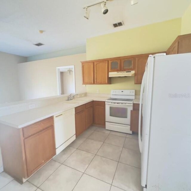 kitchen featuring visible vents, a peninsula, white appliances, under cabinet range hood, and a sink
