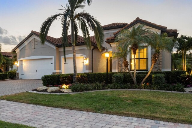 mediterranean / spanish-style home with a tiled roof, decorative driveway, a front lawn, an attached garage, and stucco siding