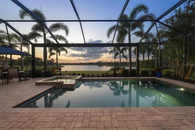 pool at dusk with a water view, a pool with connected hot tub, a lanai, and a patio area