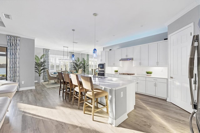 kitchen with crown molding, appliances with stainless steel finishes, light countertops, visible vents, and a center island with sink