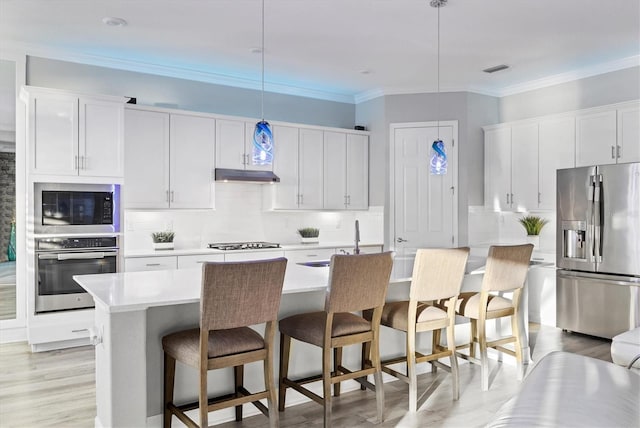 kitchen with decorative backsplash, light countertops, under cabinet range hood, a sink, and appliances with stainless steel finishes
