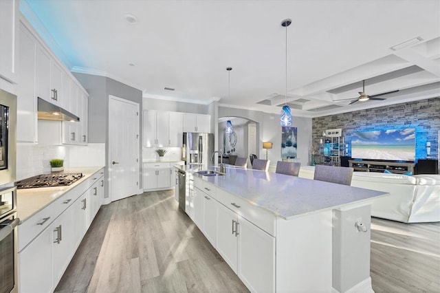 kitchen featuring a sink, open floor plan, under cabinet range hood, a ceiling fan, and appliances with stainless steel finishes