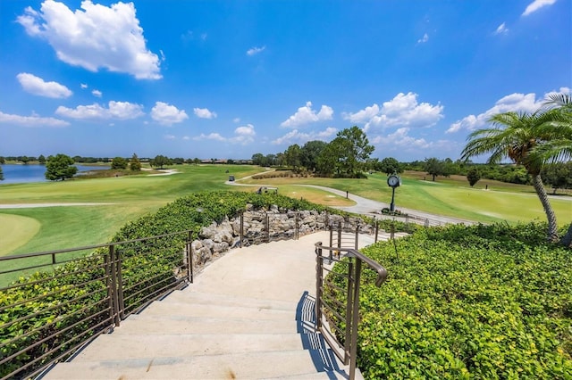 view of property's community featuring a lawn, a water view, view of golf course, and fence