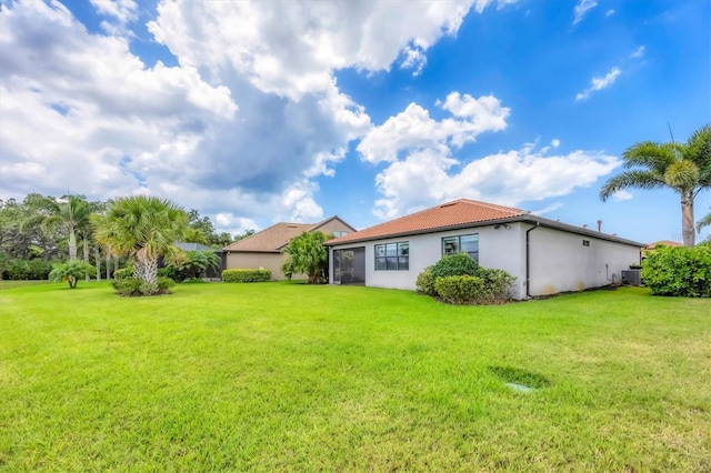 rear view of property featuring stucco siding, a yard, central AC, and a tile roof