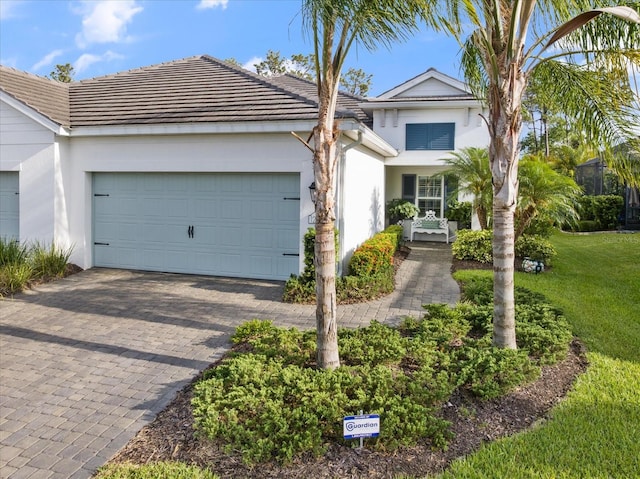 view of front facade with decorative driveway, a garage, stucco siding, and a tiled roof