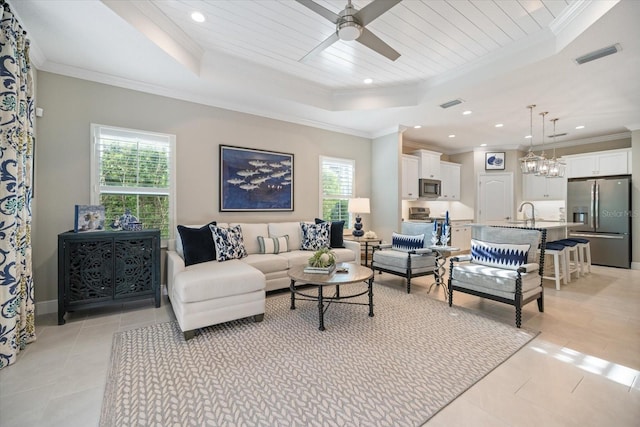 living room featuring a tray ceiling, visible vents, ornamental molding, and ceiling fan with notable chandelier