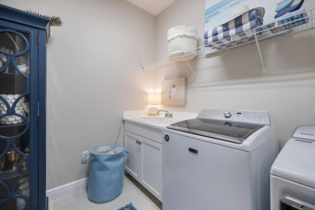clothes washing area with cabinet space, a sink, baseboards, light tile patterned flooring, and washer and dryer