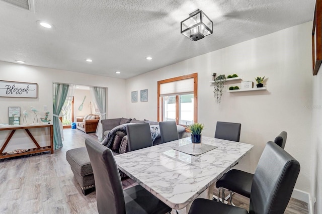 dining space with light wood-style floors, recessed lighting, a textured ceiling, and visible vents