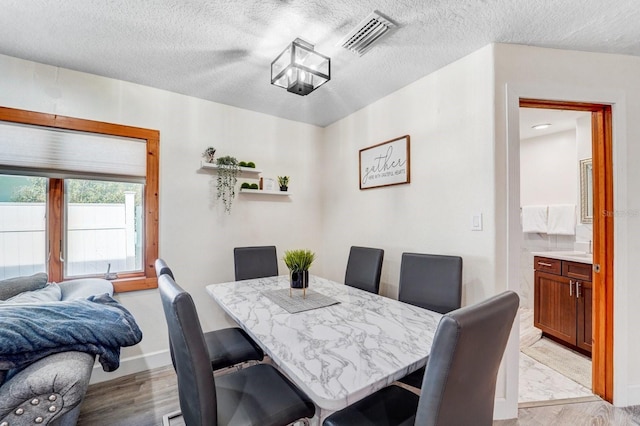 dining area featuring baseboards, light wood finished floors, a textured ceiling, and visible vents