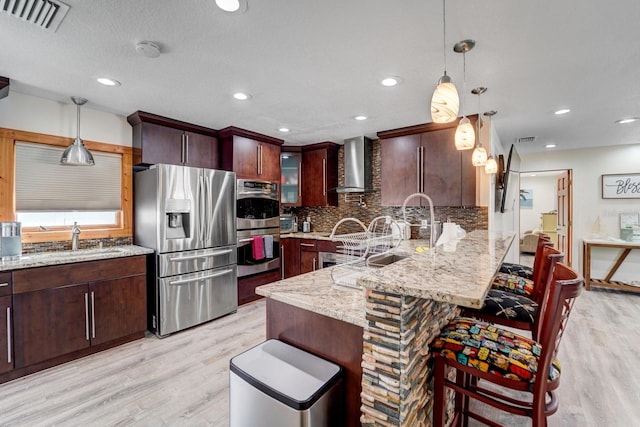 kitchen featuring wall chimney range hood, visible vents, appliances with stainless steel finishes, light wood-type flooring, and a peninsula
