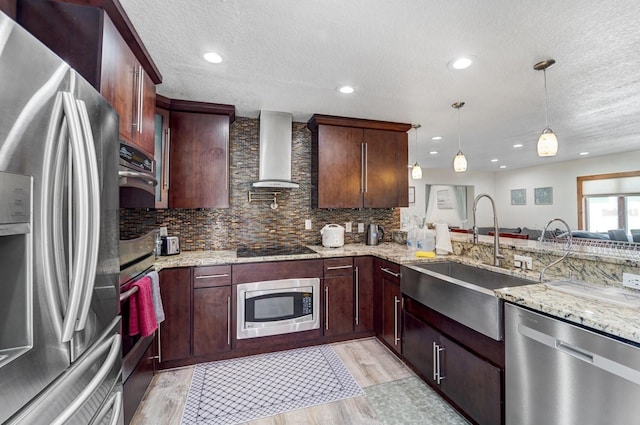 kitchen featuring wall chimney range hood, a textured ceiling, a sink, light wood finished floors, and stainless steel appliances