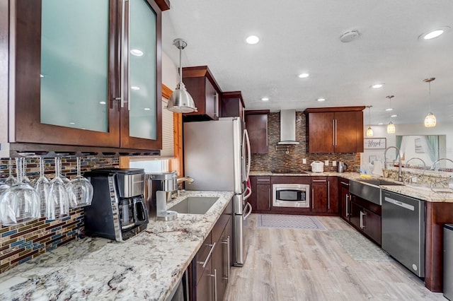 kitchen featuring a peninsula, appliances with stainless steel finishes, decorative backsplash, and wall chimney exhaust hood