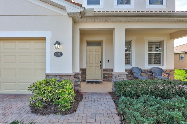 view of exterior entry featuring a garage, stucco siding, a porch, and stone siding