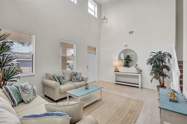 living room featuring visible vents, baseboards, a towering ceiling, and wood finished floors