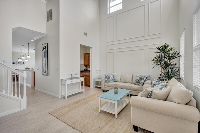living area featuring a high ceiling, visible vents, baseboards, and light wood-style floors