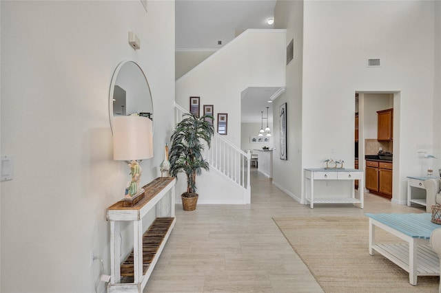 hall with stairway, baseboards, a high ceiling, and visible vents