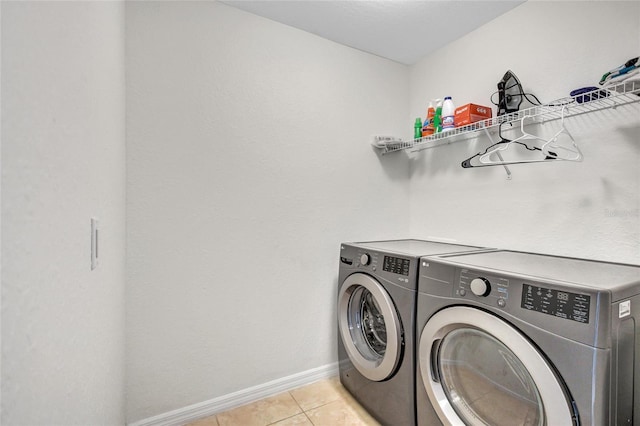clothes washing area with laundry area, baseboards, washing machine and dryer, and light tile patterned flooring