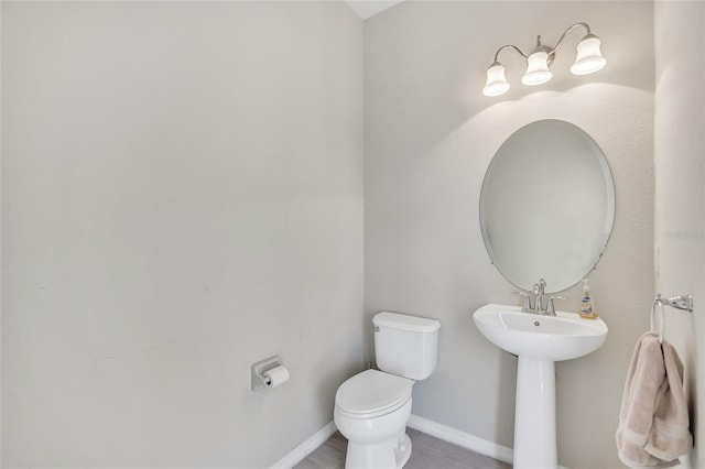 bathroom with baseboards, wood finished floors, and toilet