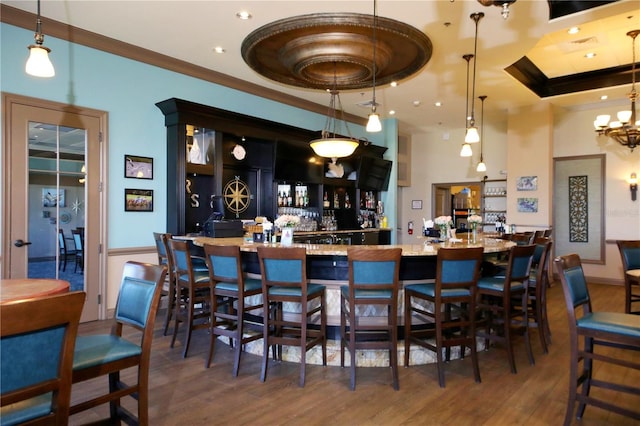 bar featuring crown molding, a community bar, pendant lighting, and wood finished floors