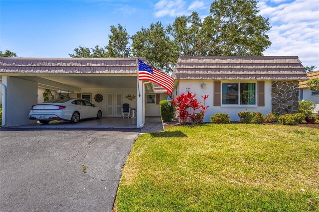 view of front of home with a front yard, a carport, mansard roof, aphalt driveway, and stucco siding