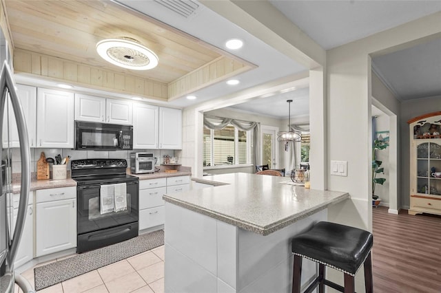 kitchen with a kitchen breakfast bar, ornamental molding, black appliances, and white cabinetry
