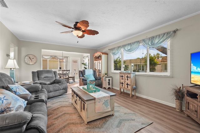 living room with crown molding, light wood-style flooring, a ceiling fan, baseboards, and visible vents
