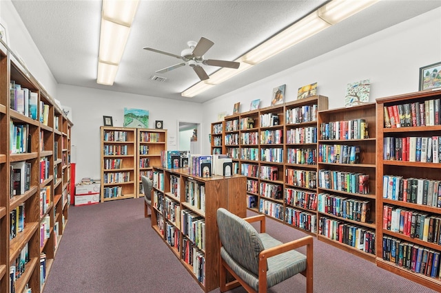 living area with wall of books, a ceiling fan, carpet, and visible vents
