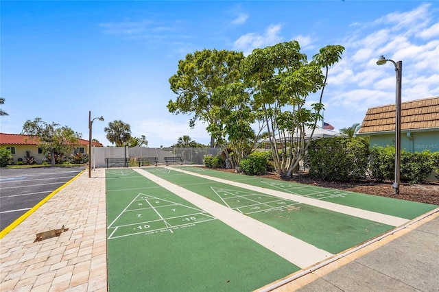 view of community with uncovered parking, fence, and shuffleboard