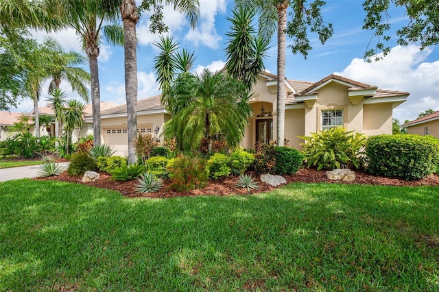 mediterranean / spanish-style home featuring a tiled roof, an attached garage, a front yard, and stucco siding
