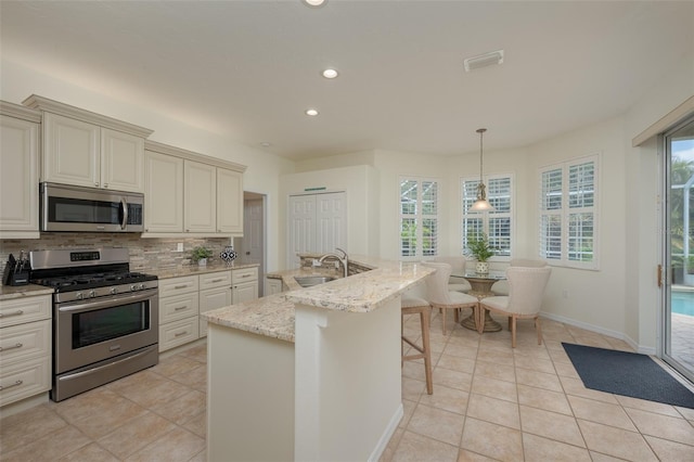 kitchen with appliances with stainless steel finishes, tasteful backsplash, light stone counters, recessed lighting, and light tile patterned flooring