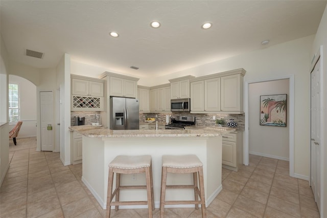 kitchen with a kitchen island with sink, visible vents, tasteful backsplash, light stone countertops, and stainless steel appliances