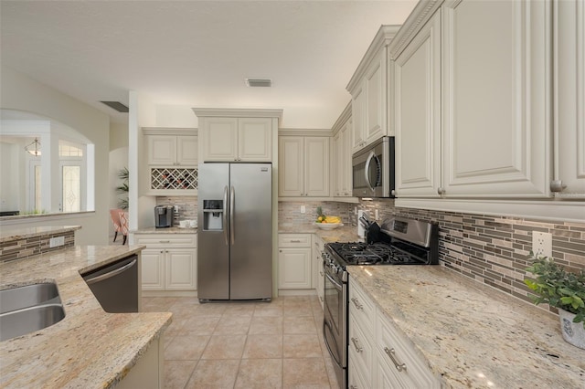 kitchen with backsplash, light stone countertops, appliances with stainless steel finishes, and visible vents