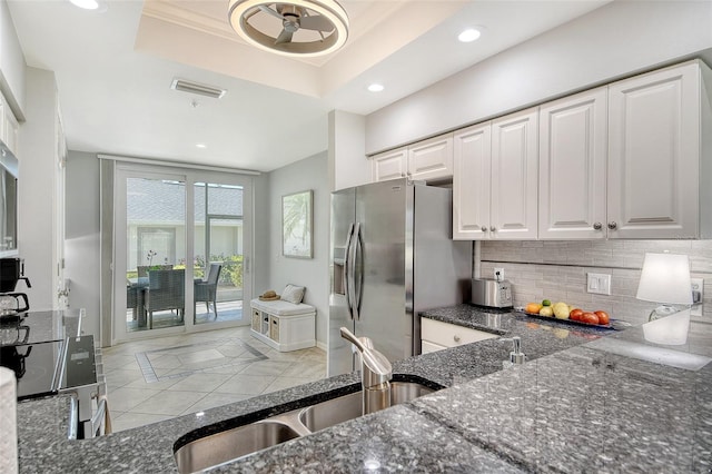 kitchen with stainless steel fridge, a sink, a raised ceiling, dark stone counters, and recessed lighting