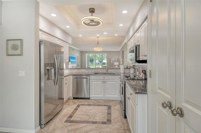 kitchen with dark stone counters, a tray ceiling, white cabinets, hanging light fixtures, and stainless steel appliances