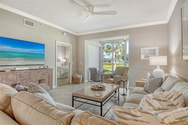 tiled living area with ceiling fan, a textured ceiling, baseboards, visible vents, and ornamental molding