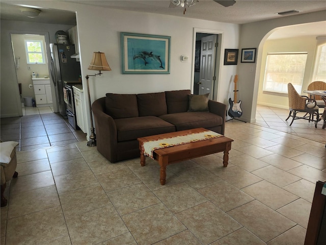 living room with arched walkways, light tile patterned floors, and a ceiling fan