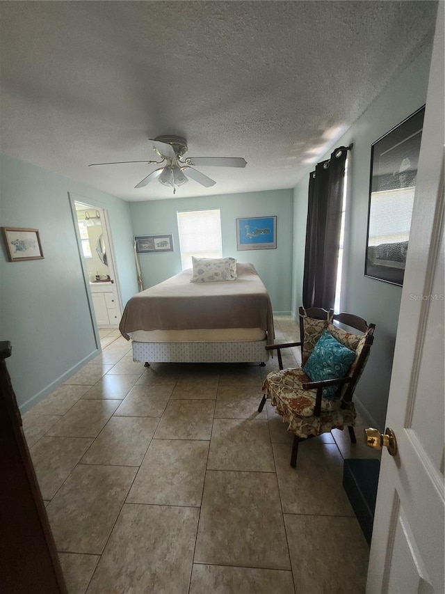 bedroom featuring tile patterned flooring, a ceiling fan, ensuite bath, a textured ceiling, and baseboards