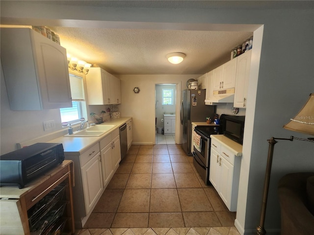 kitchen with a sink, under cabinet range hood, appliances with stainless steel finishes, white cabinets, and a textured ceiling
