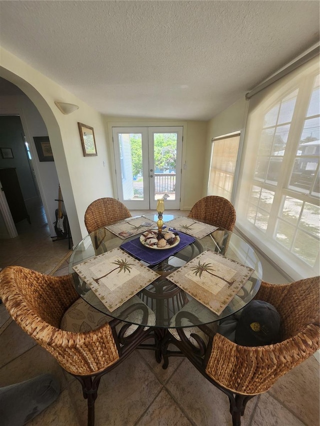 dining area with arched walkways, a textured ceiling, and french doors