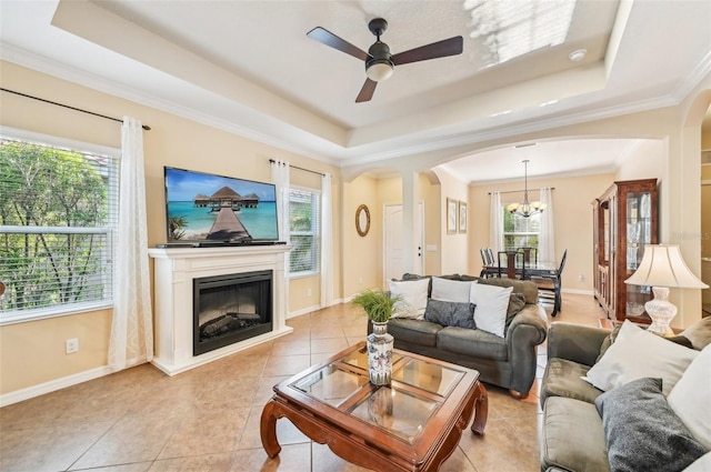 living area with a tray ceiling, arched walkways, a ceiling fan, tile patterned flooring, and a glass covered fireplace