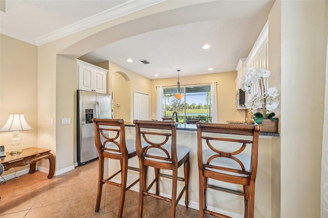 kitchen featuring stainless steel fridge, arched walkways, a peninsula, a breakfast bar, and white cabinets