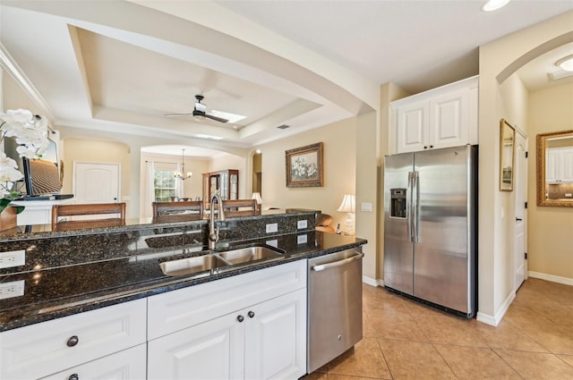 kitchen with appliances with stainless steel finishes, a sink, arched walkways, dark stone countertops, and ceiling fan