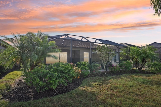 back of property at dusk with glass enclosure and a lawn